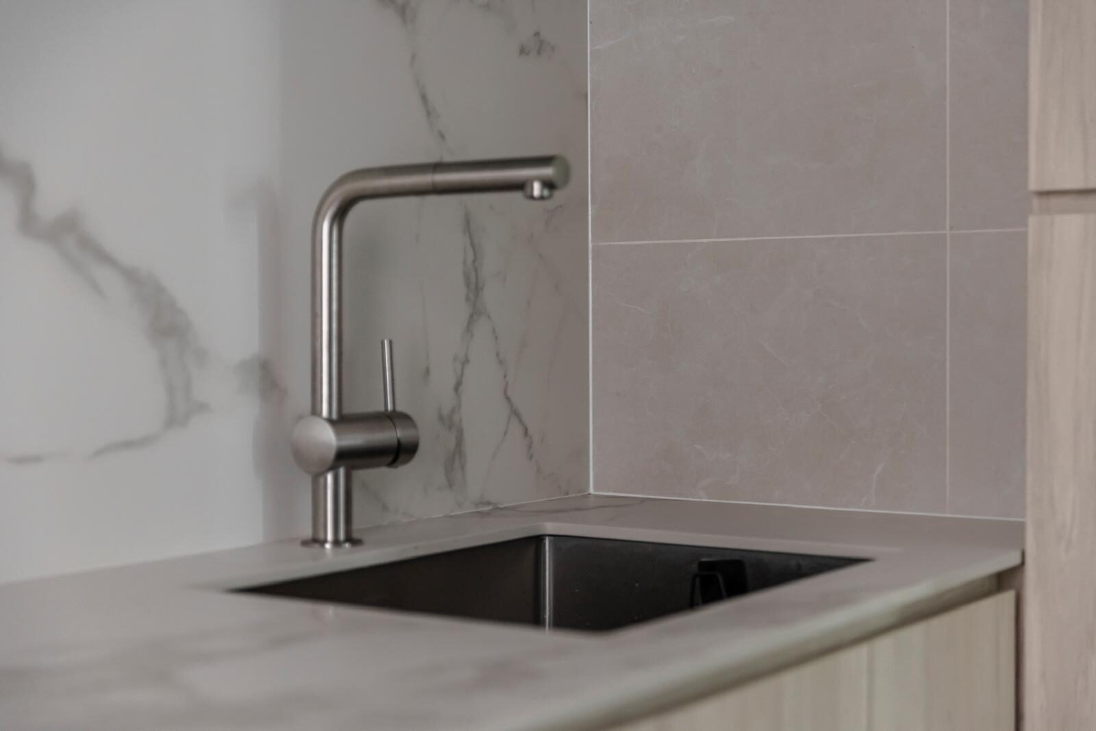 Marble splashback meeting stone-look tile at a mitred corner, kitchen interior by Porterbox Studio