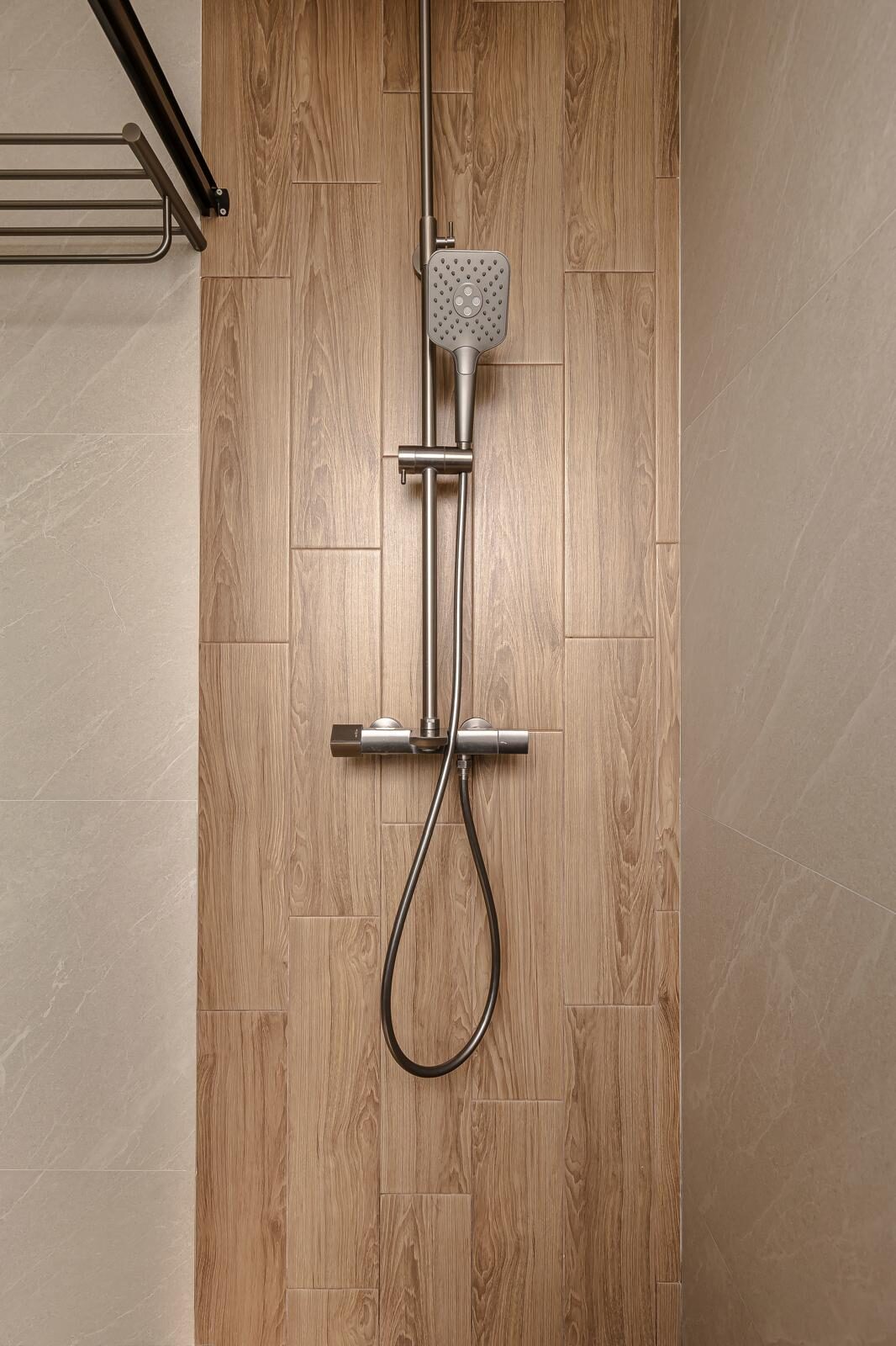 Wood-look tile band framing a brushed steel shower column, bathroom interior by Porterbox Studio